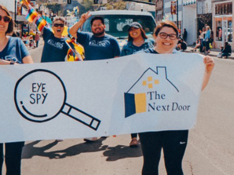 two people hold a banner saying The Next Door