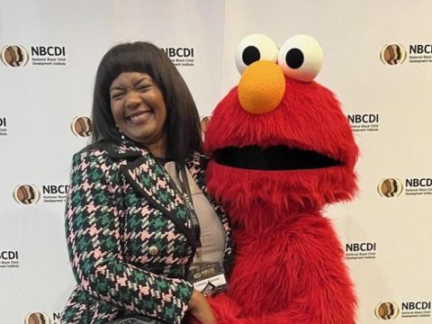 A woman smiles while hugging an Elmo character