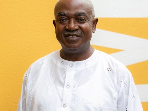 A man in a white shirt smiles with a yellow background  behind him