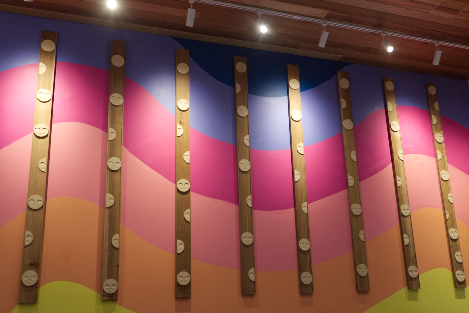 An art installation showing a wavy rainbow color adorned with many smiling faces. 