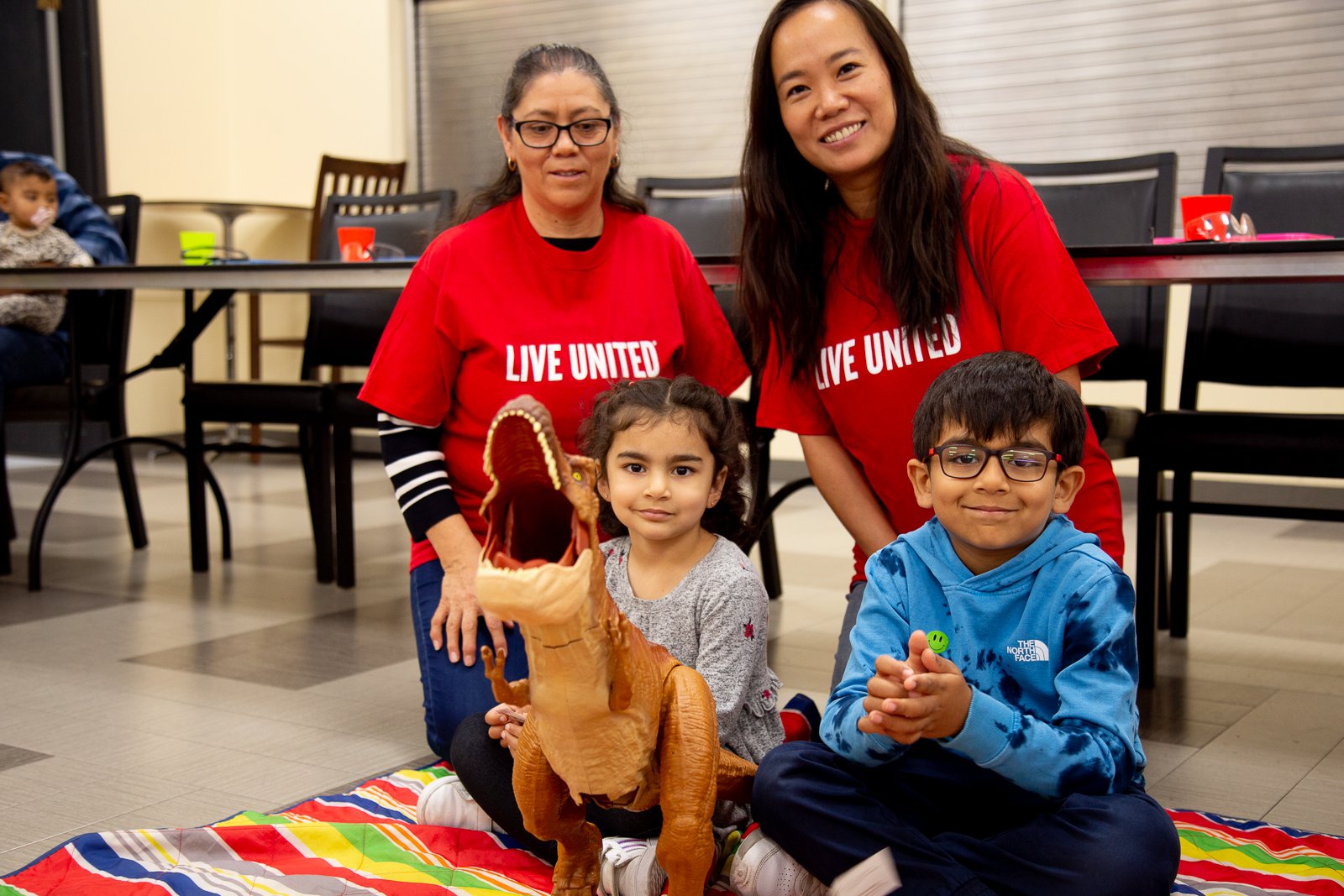 two teachers take a photo with two children and a big T-rex toy