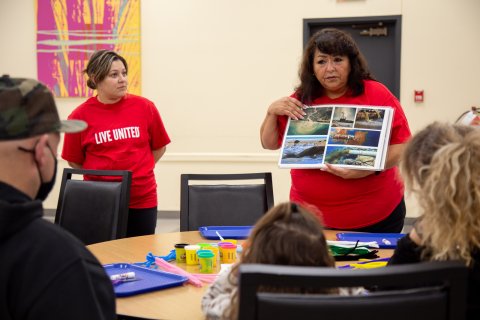 Dorila flips through a book, showing a group of kids and parents its images. 