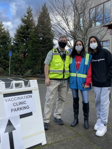 Three volunteers stand by a sign informing people of COVID testing