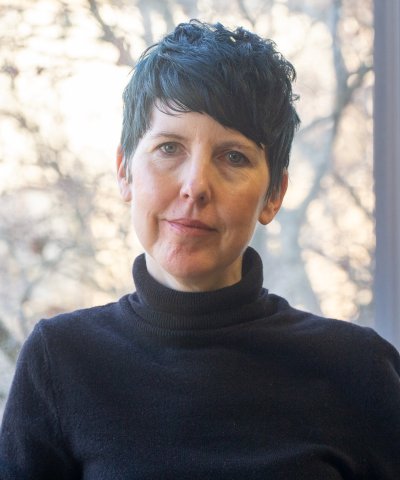 A woman standing in front of a window looks at the camera