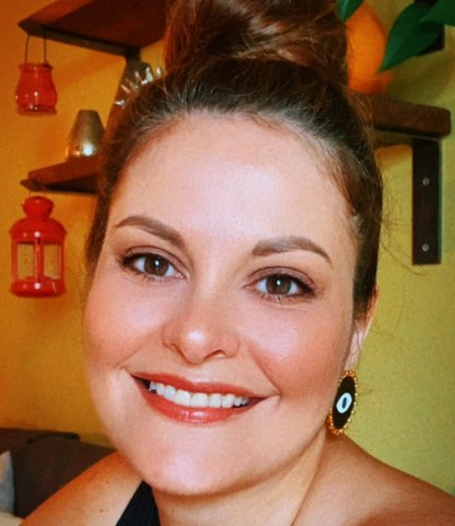 A woman smiles at the camera in a black top with her hair up