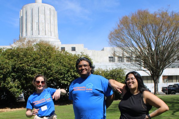Three people lock arms in front of the Oregon State Capitol Building