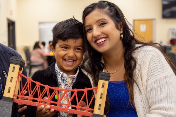 A child and his mother smile for the camera while holding a toy bridge