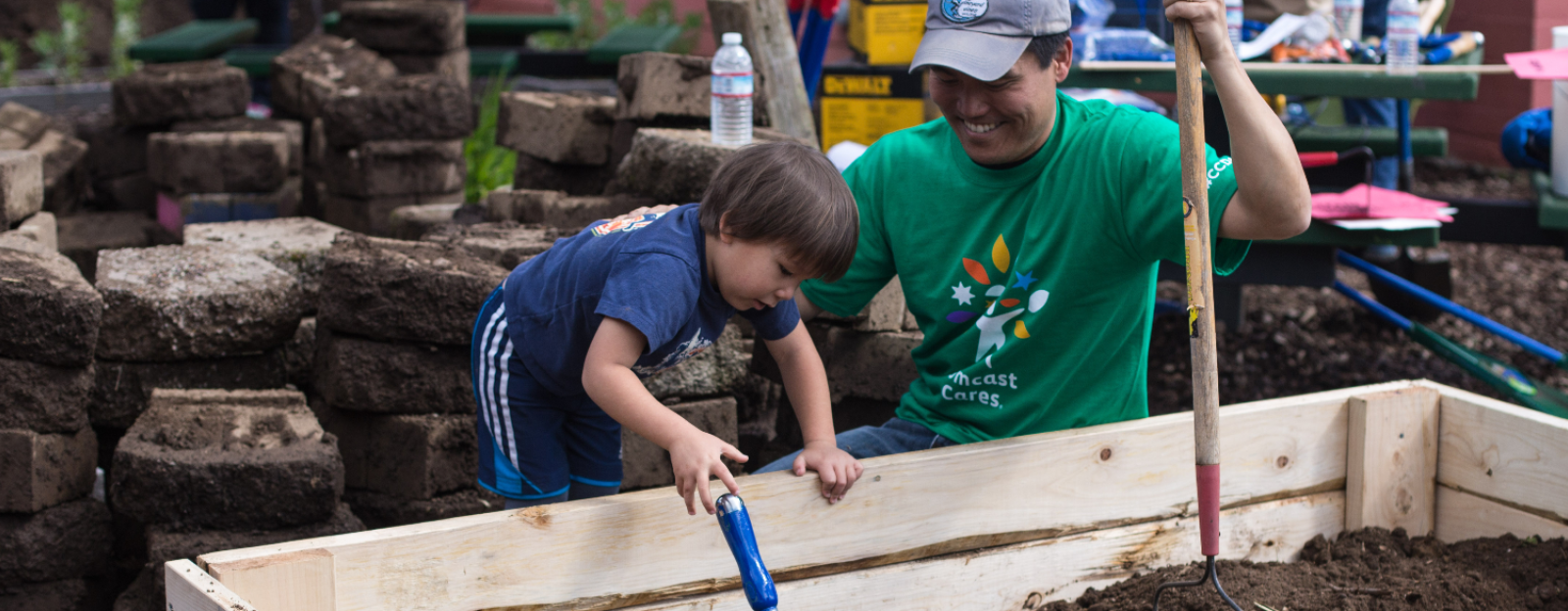 A man in a green shirt helps a child work in a garden bed. 