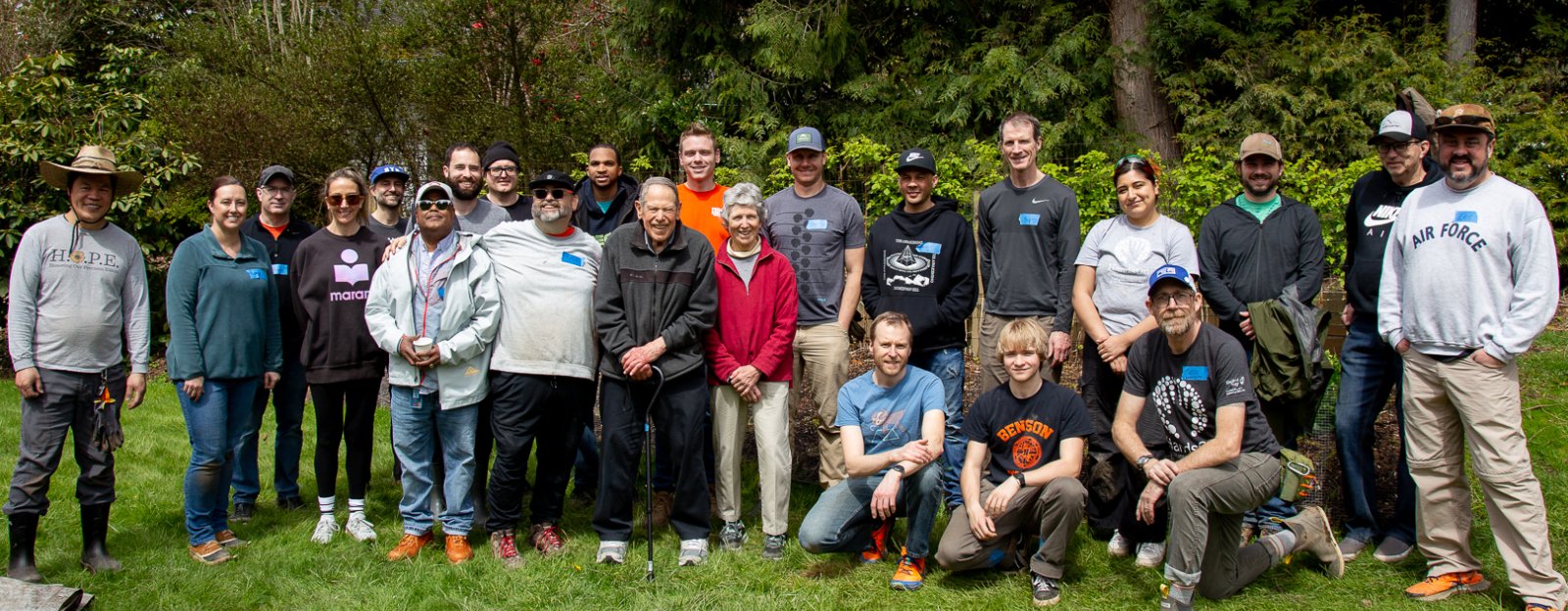 A large group of Nike employees pose with two elderly people in a green field of grass with trees behind them