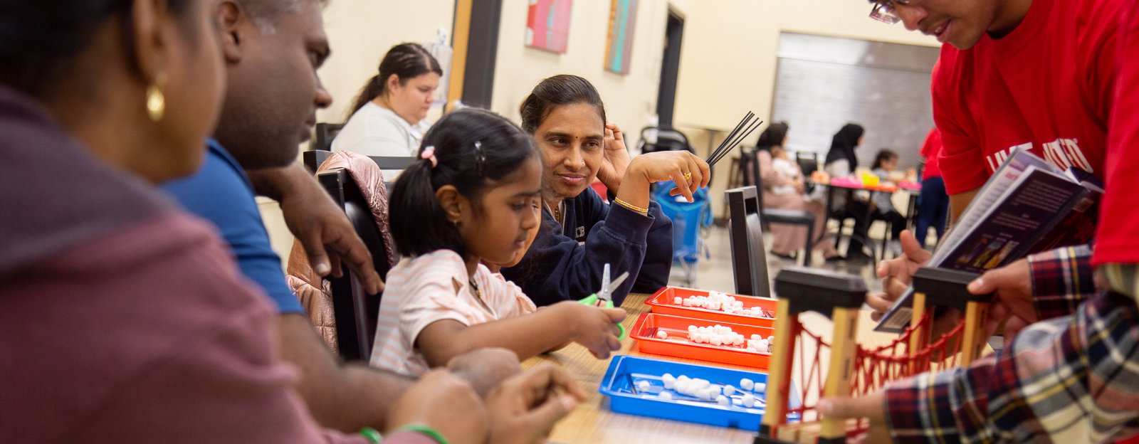 A teacher in a red United Way shirt shows children and parents a book