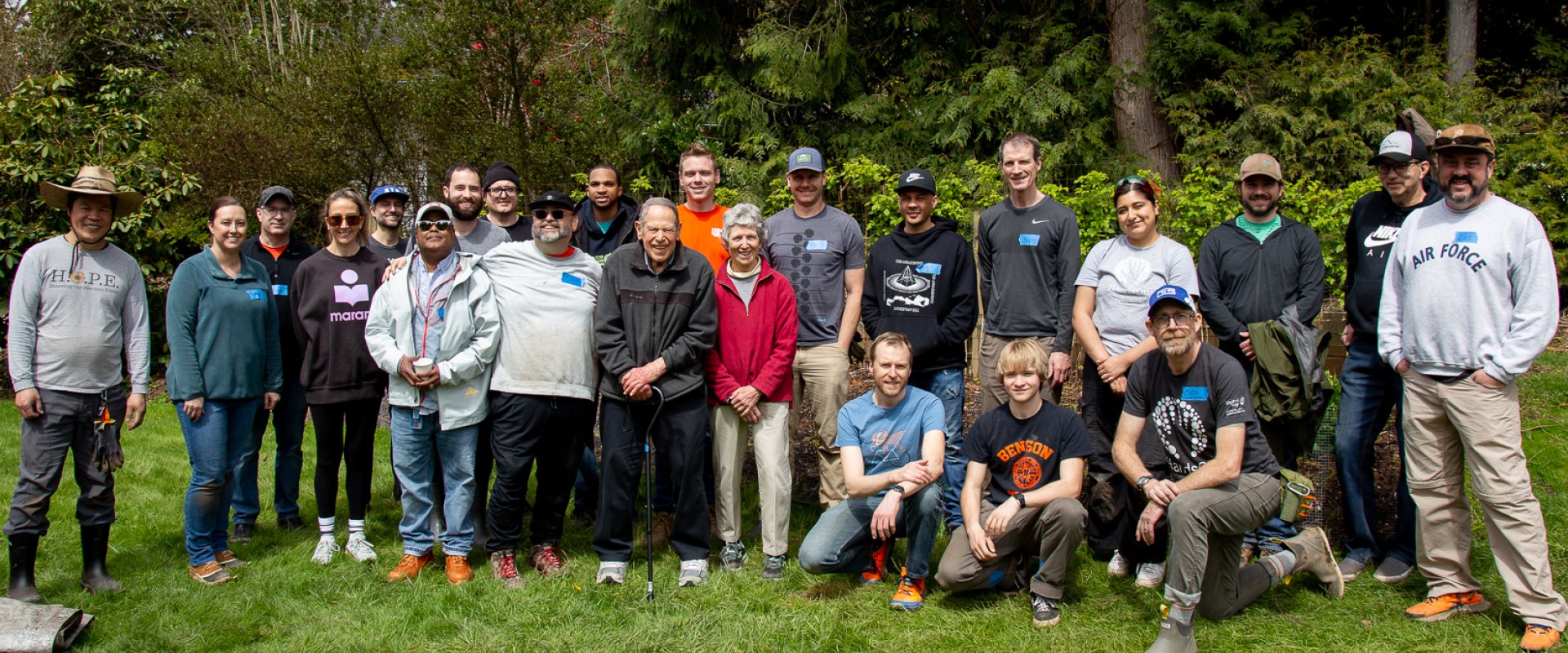 A large group of Nike employees pose with two elderly people in a green field of grass with trees behind them