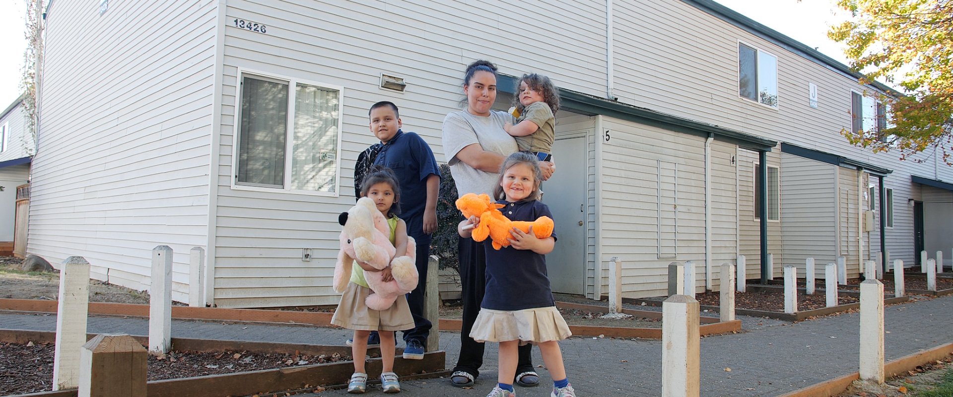 A family hugging in front of an apartment complex