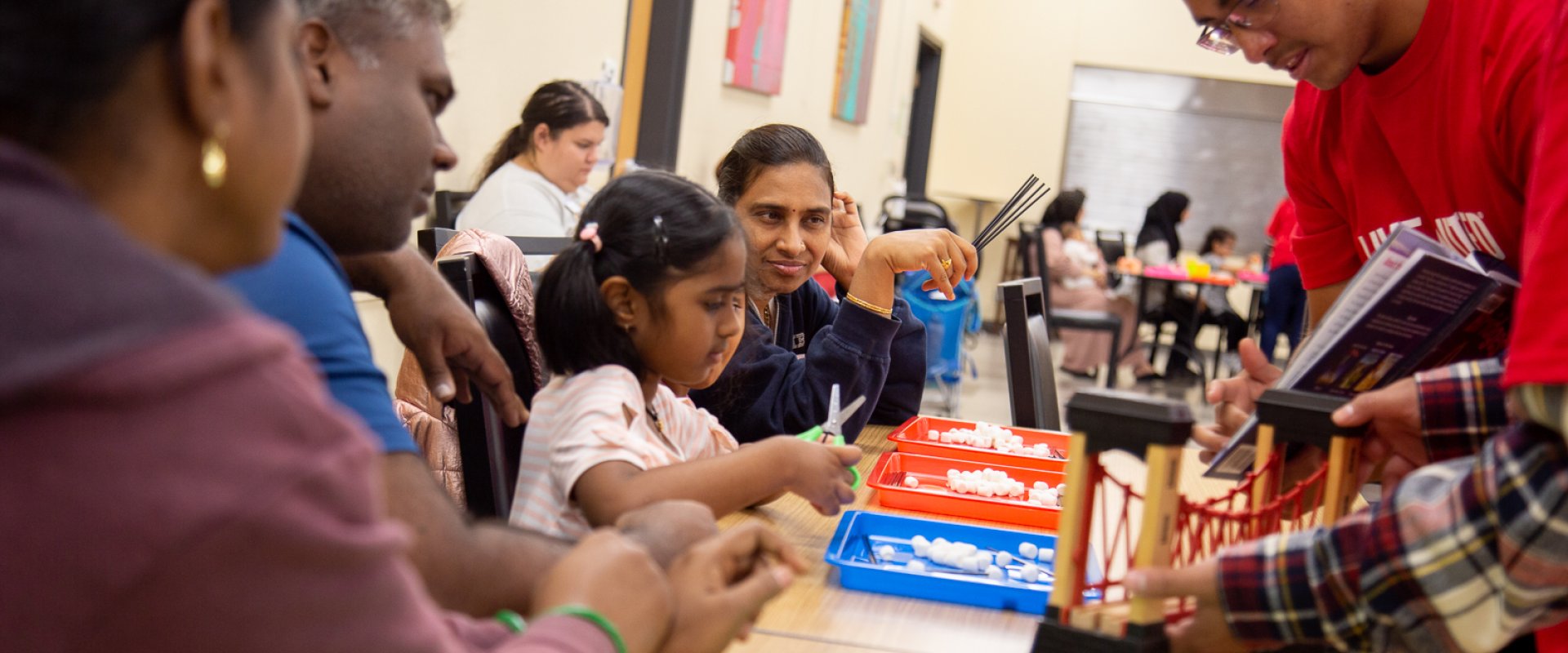 A teacher in a red United Way shirt shows children and parents a book