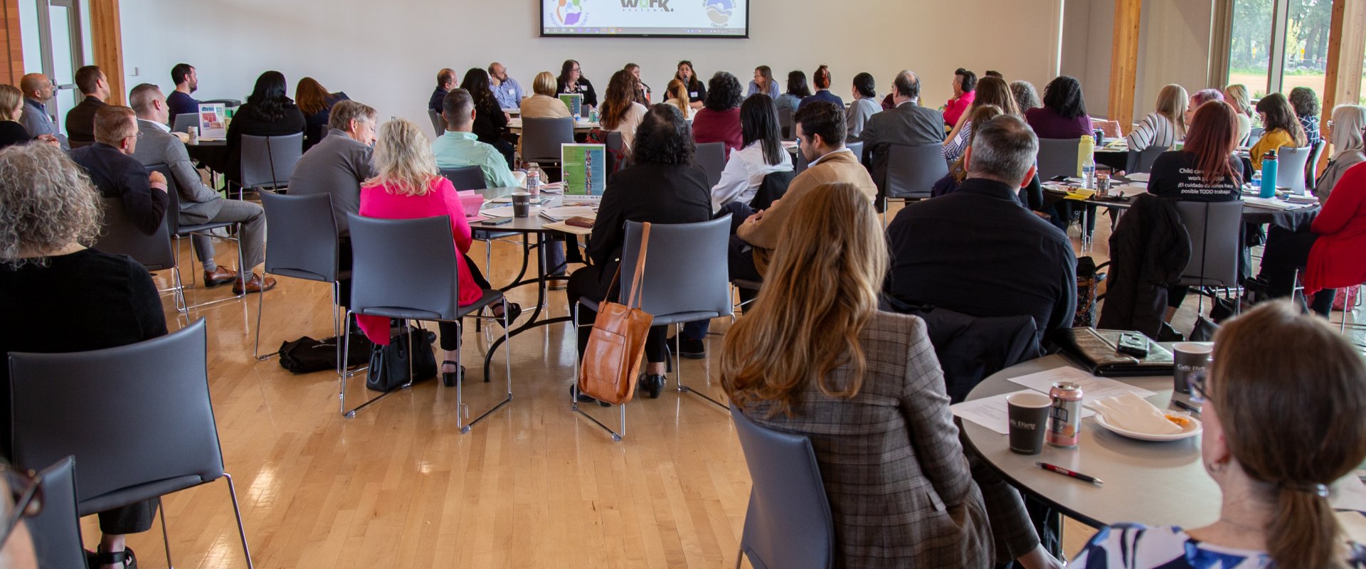 A crowded room with speakers in the front and a projector screen