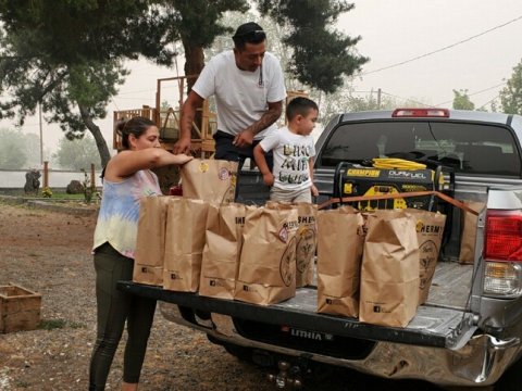 Family loading boxes and supplies into the back of a pickup; sky is hazy & smoky