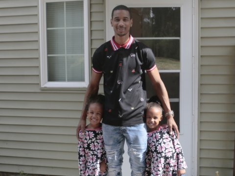 a man hugging his two daughters in front of a home