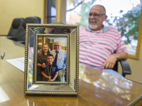 A man sits behind a desk that has a photo of him and his family in focus