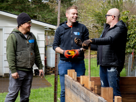 Three men talk over a raised garden bed