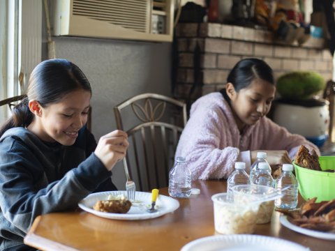 Two young girls eating dinner at table.