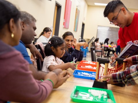 A man teaches a group of children and parents with a book