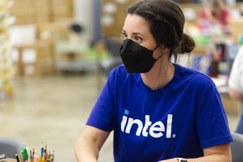 A woman in a blue shirt that says intel. She wears a M95 mask in what looks to be a schoolroom