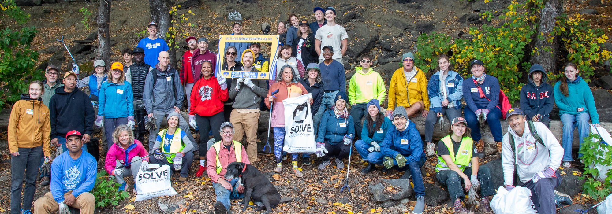 A large group of people pose with trash bags and tools 