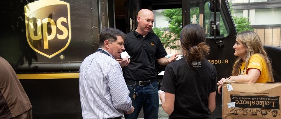 a woman with her back to the camera looks on at a UPS truck. She has a United Way of the COlumbia-Willamette logo on her shirt