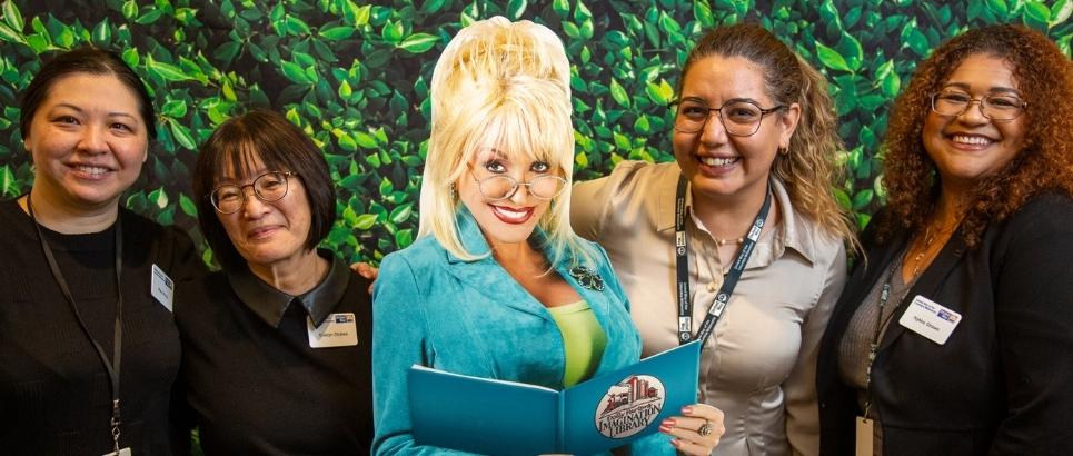four people stand with a dolly parton cutout smiling