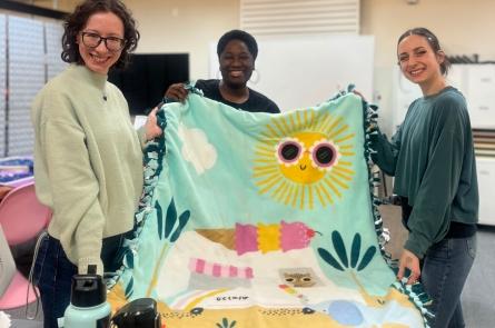 A group of three people work on a blanket