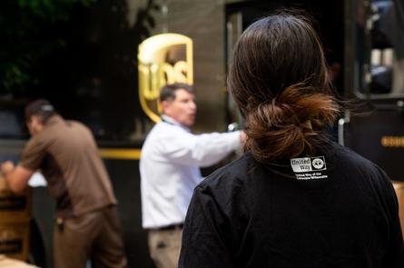 a woman with her back to the camera looks on at a UPS truck. She has a United Way of the COlumbia-Willamette logo on her shirt