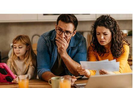 Parents (mom and dad) looking at bills with faces of concern. Daughter is sitting next to them looking at an iPad.
