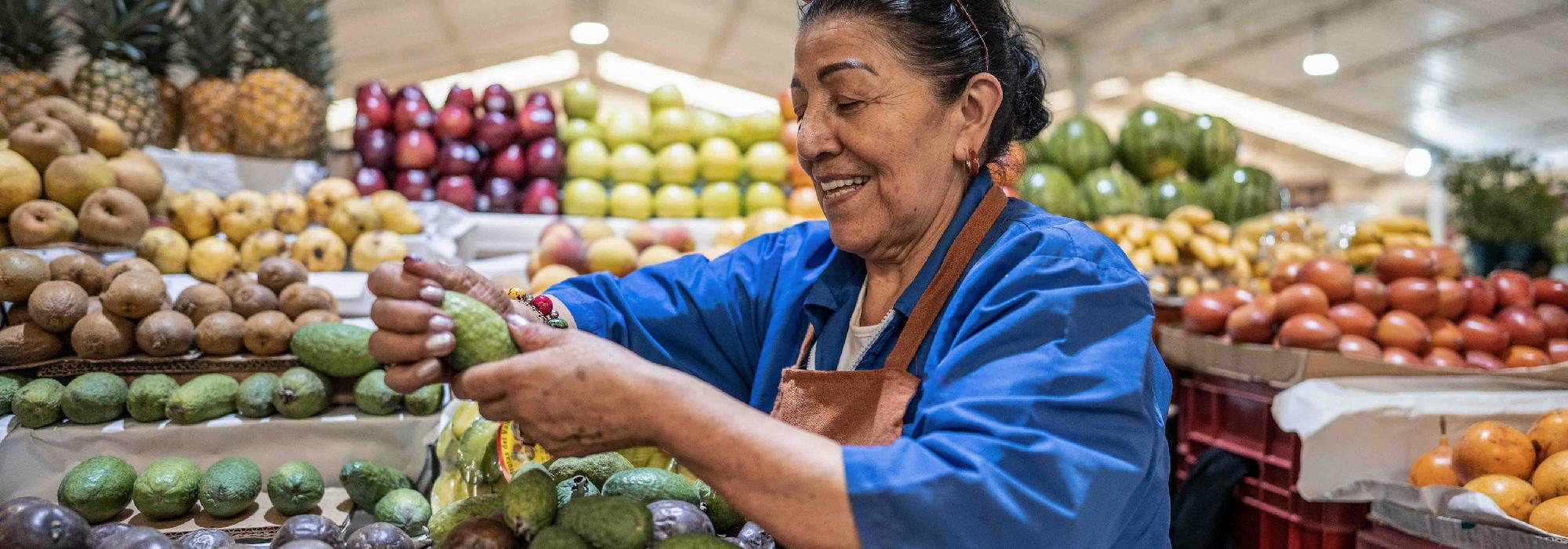 A woman in a grocery store smiles as she looks at avocados