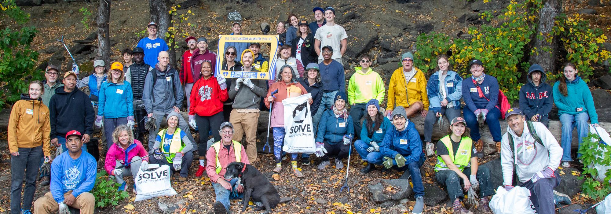 A large group of people pose with trash bags and tools 