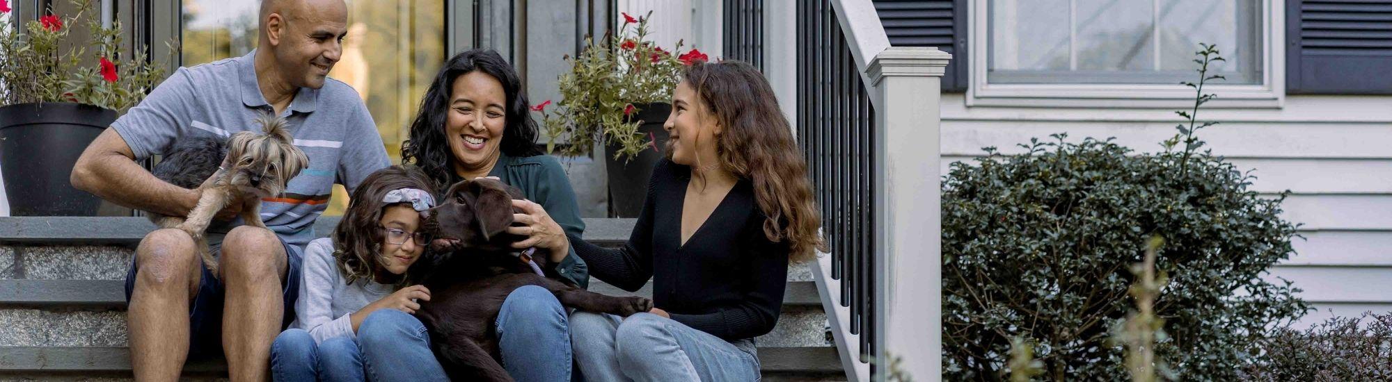 A family sits on the steps of a home enjoying themselves. Several dogs sit with them