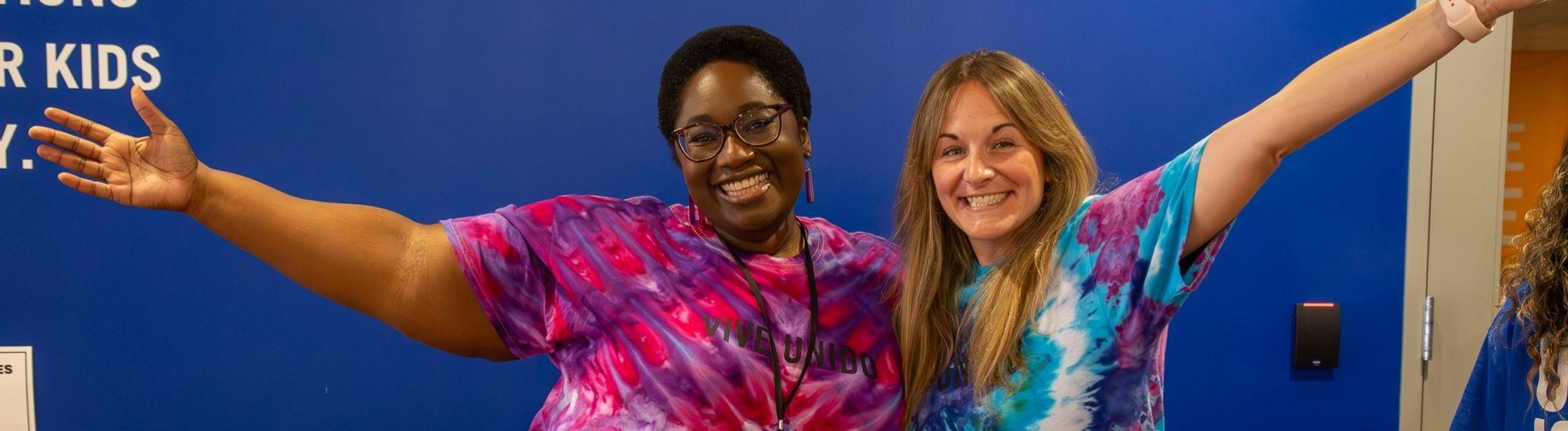 Two women smile and stretch their arms out